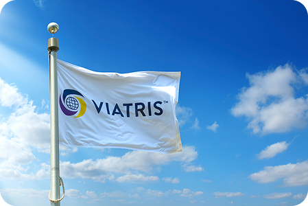  Bandiera con logo Viatris sventola al vento su cielo azzurro, simbolo dell’impegno globale dell’azienda farmaceutica nella produzione di farmaci equivalenti sicuri e di qualità.